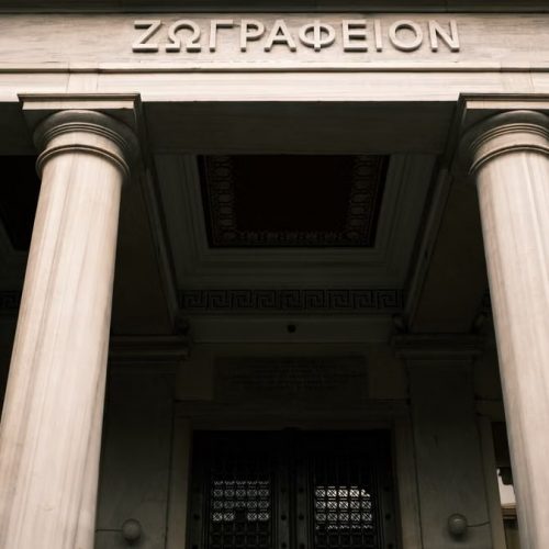 Low angle view of a historical building facade with Greek columns and inscriptions.