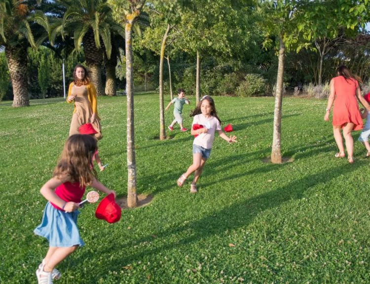 Kids and adults enjoy playing together in a lush, sunny park setting.